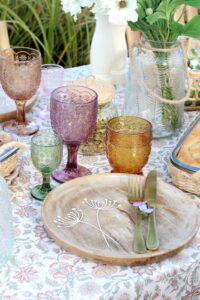 pöydällä on viinilaseja eri värissä, puinen tarjotin ja kukat maljakossa