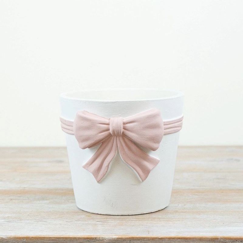 valkoinen keraaminen ruukku koristeltu vaaleanpunaisella rusetilla seisoo pöydällä