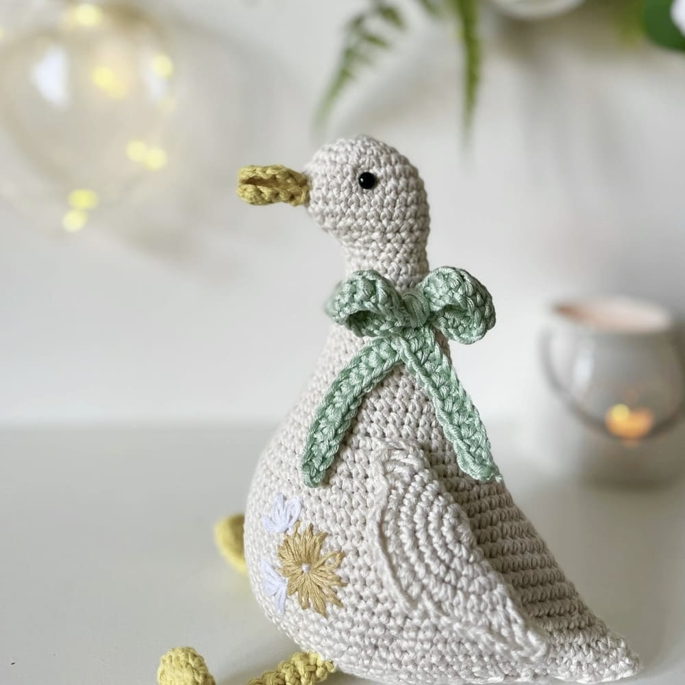 Käsin virkattu valkoinen pääsiäiskana ja koristeltu rusetilla istuu hyllyllä