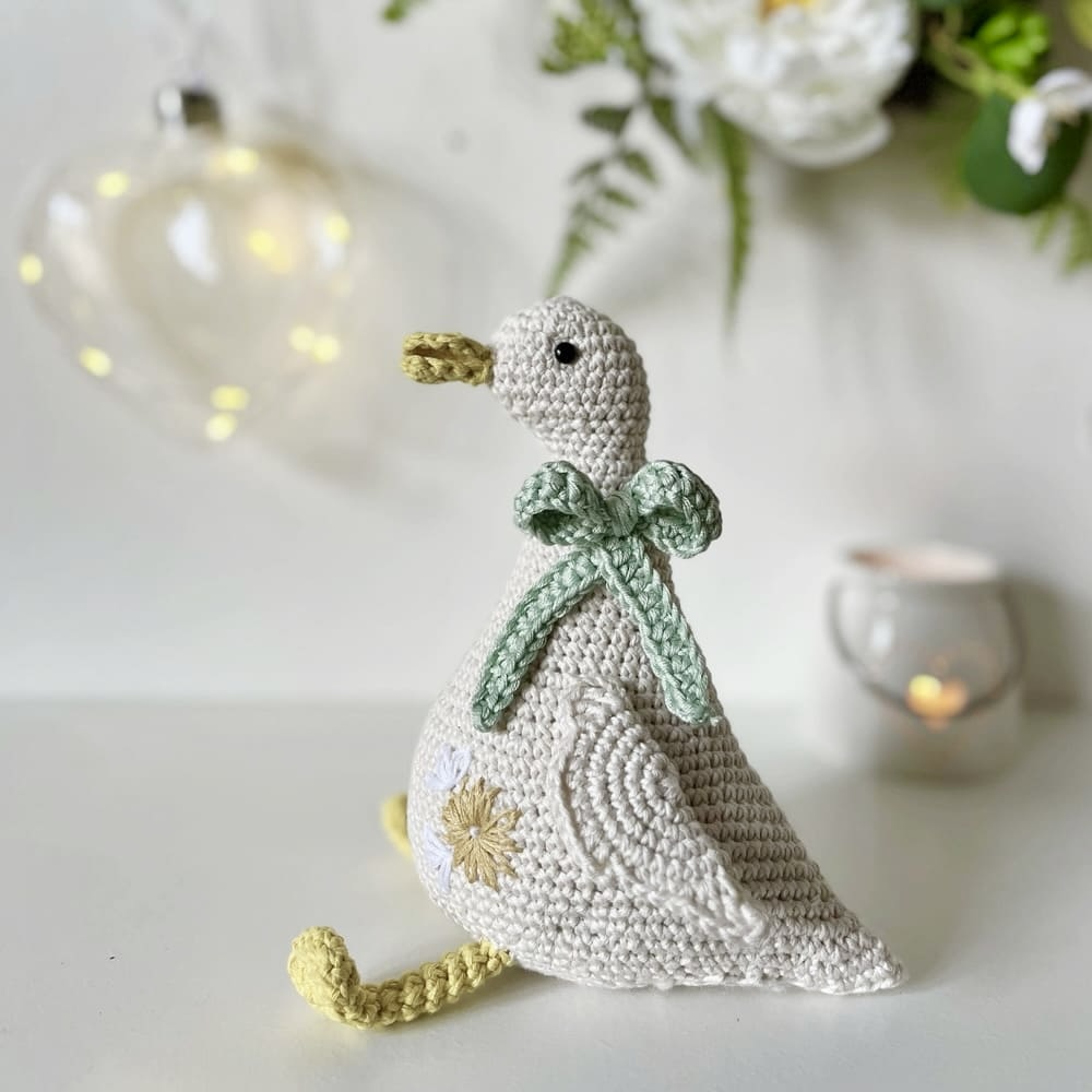 pääsiäiskoriste käsin virkattu hanhi rusetilla istuu hyllyllä muiden esineiden kanssa